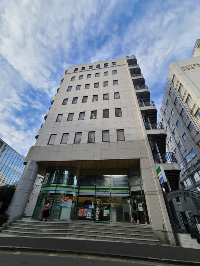 現代的な建物のファサードで、ファミリーマートのコンビニエンスストアが入っている、青空と雲が背景の風景