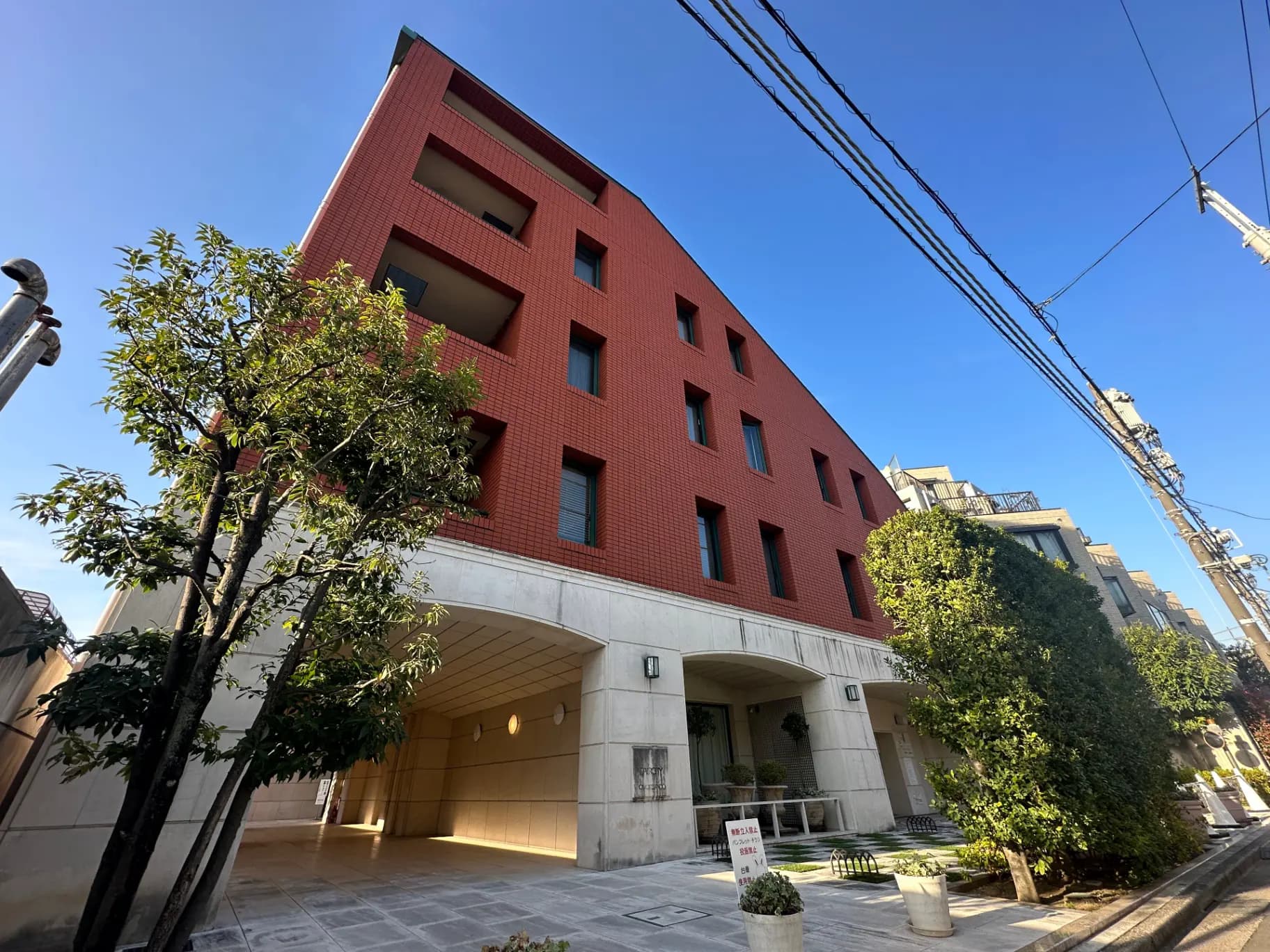 赤レンガの外壁が特徴的なモダンな建築物、植栽された緑と開放的なエントリーエリアが見えるマンションの外観
