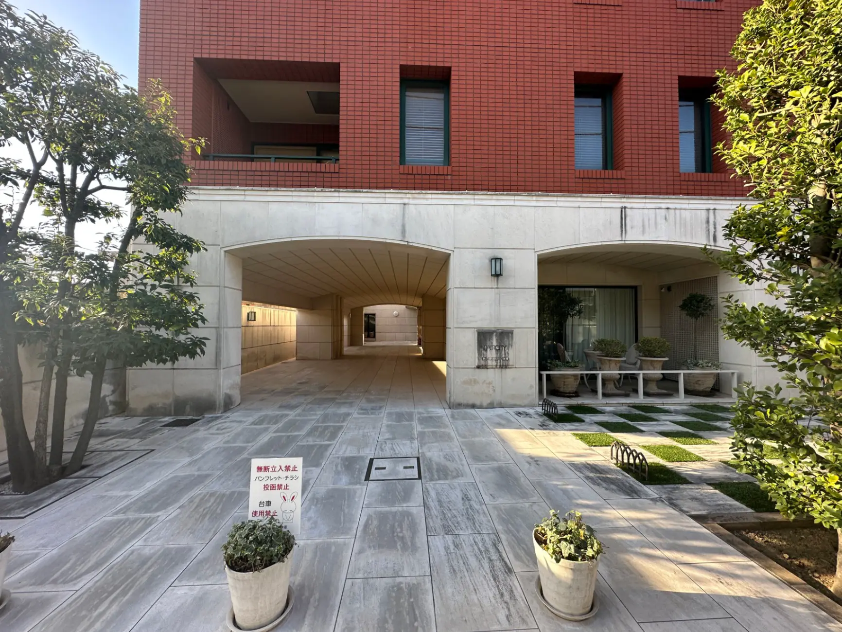 赤レンガの外壁を持つモダンなアパート建物、アーチ形の通路と緑豊かな植栽があるエントランスエリア