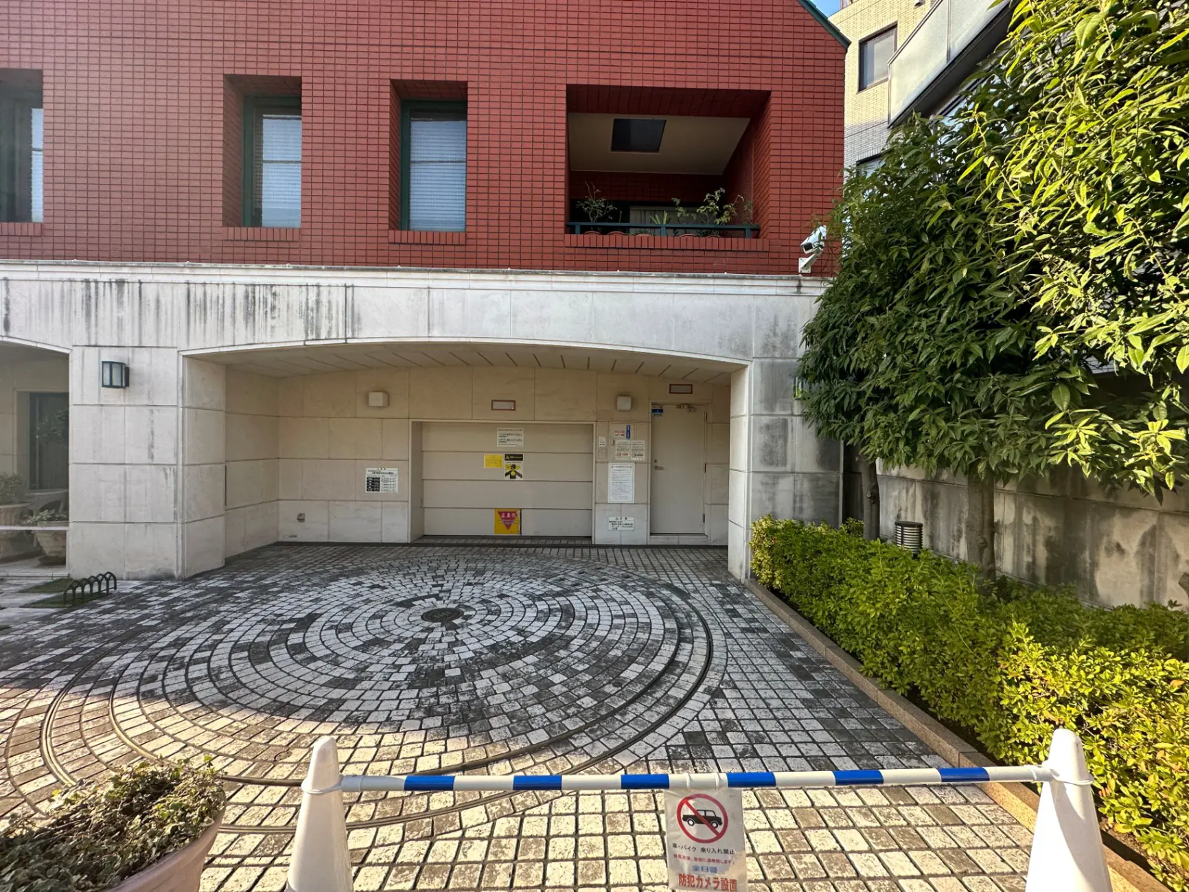 レンガ造りのマンションのエントランス、車両進入禁止のバー、円形のモザイクタイルデザインの庭園