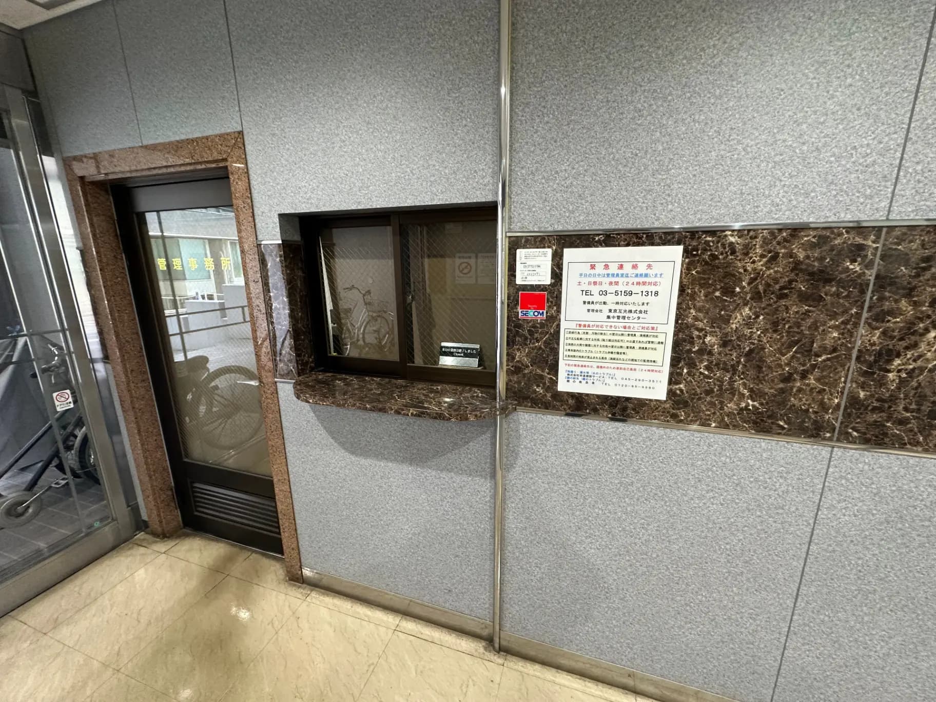 ビルのエントランスに設置されたインフォメーションボックスと掲示板、自動扉と駐輪スペースが見えるオフィスエントリーウェイ