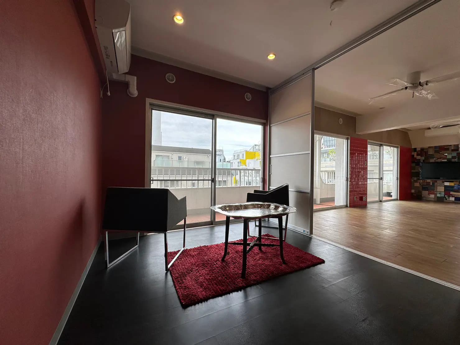 モダンなインテリアのリビングルーム、茶色のアクセント壁、ガラステーブルと赤いラグが置かれた部屋、バルコニーアクセス付き