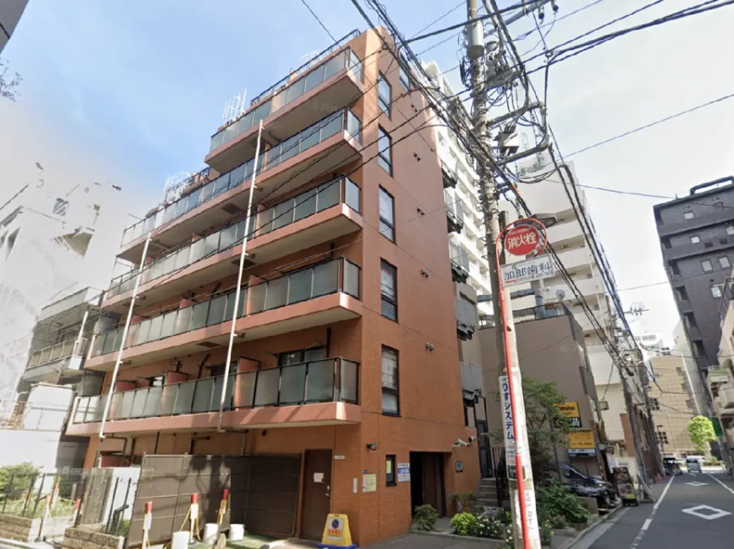- 鉄筋コンクリート造の5階建てマンション、バルコニーがついた外観、周辺に高いビルが立ち並ぶ都市部の風景