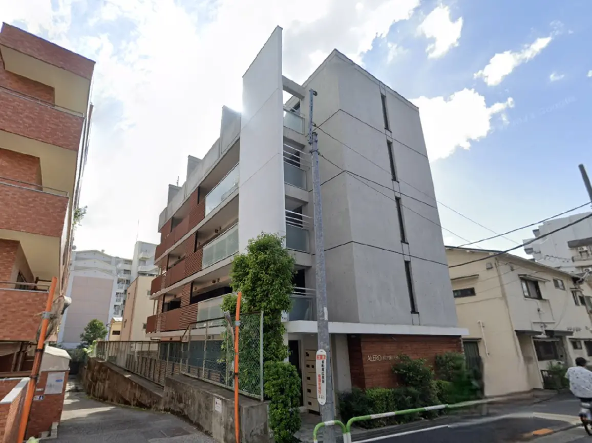 - モダンなデザインのアパートメントビル、隣接するレンガ造りの建物と緑の植栽がある外観