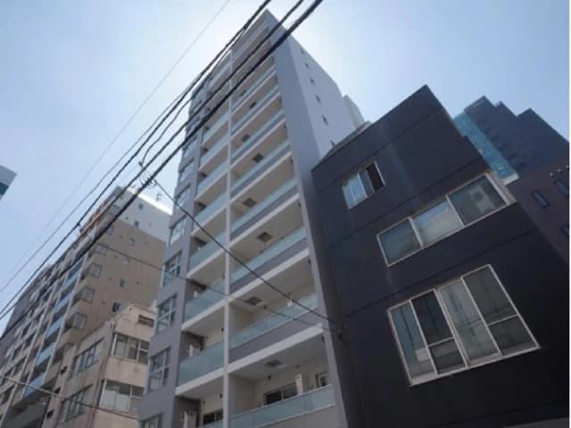 - 高層ビルの外観、青空をバックにした現代的なデザインのマンション、周囲には他の建物や電線が見えるシーン