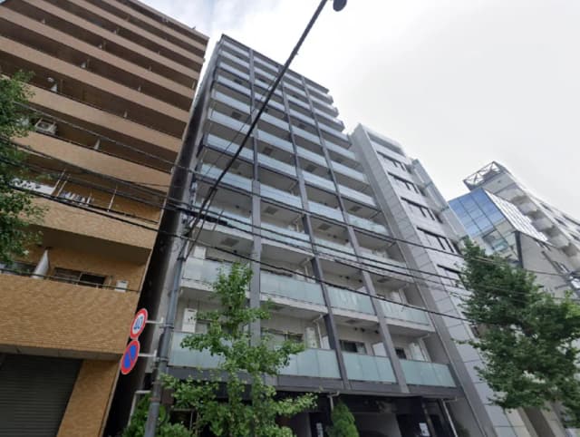 - モダンなマンションの外観、広いバルコニーとガラス手すりを持つ高層ビル、周囲には緑の木々と電柱が見える住宅街の風景