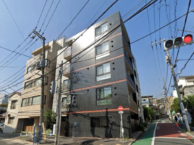 - 黒いタイル張りの現代的な外観を持つマンション、周囲には電線や交通信号が見える街の風景