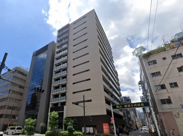 - 近代的な高層マンションの外観、青空の下で映えるガラスとコンクリートのデザイン、周囲に緑が配された街並み