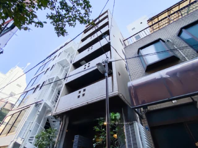 - 都会的な風景にそびえるモダンなアパートメントビル、青空の下で他の建物と隣接している様子