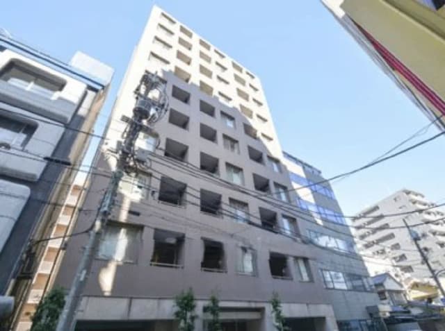 - 都市型マンションの外観、隣接する建物と電柱が見える若干高めの視点からの写真、青空が背景