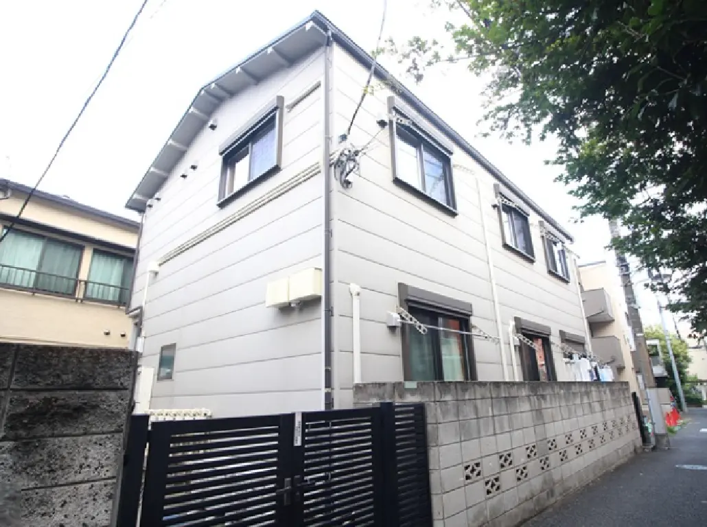 - シンプルでモダンなデザインの二階建て住宅、白い外壁と黒いフェンスが特徴的、周囲は緑に囲まれている住宅街の風景