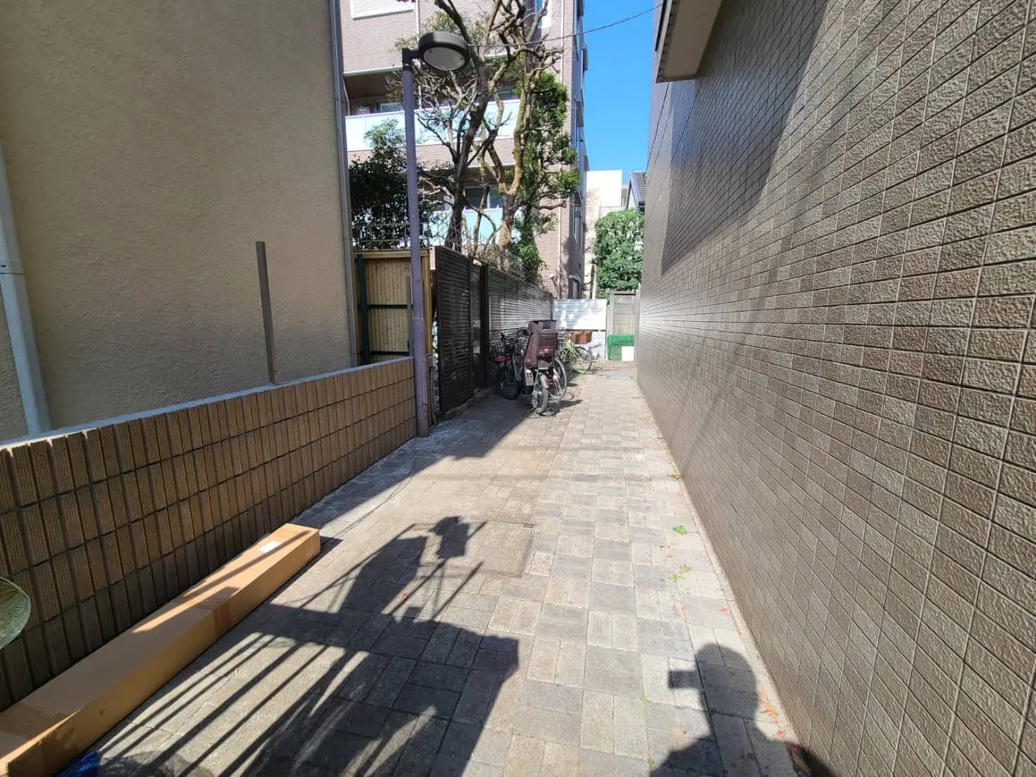日差しが降り注ぐ都市の狭い路地、壁に自転車と影