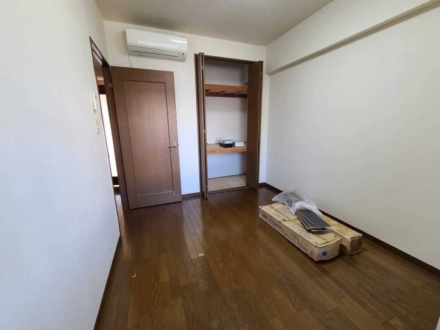 シンプルなデザインの空の部屋、木製フローリング、エアコンとクローゼットの扉が見えるインテリア