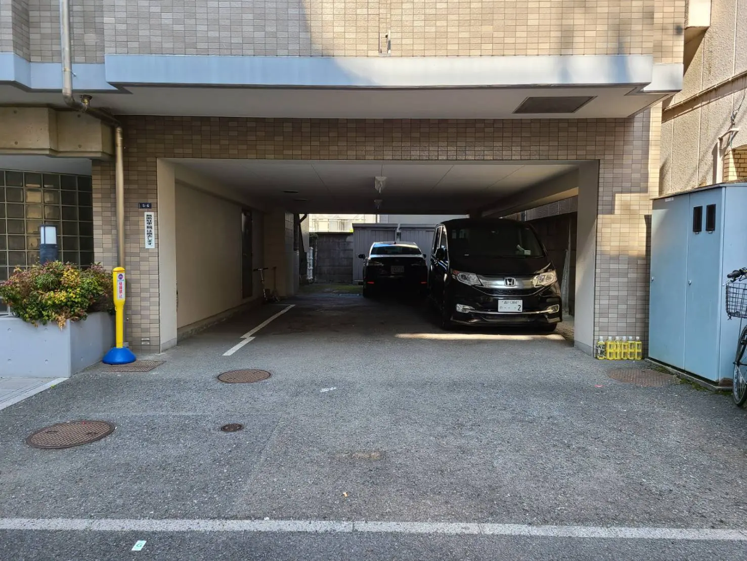 都市のマンションの共有駐車場、屋根付きで車２台が停車中