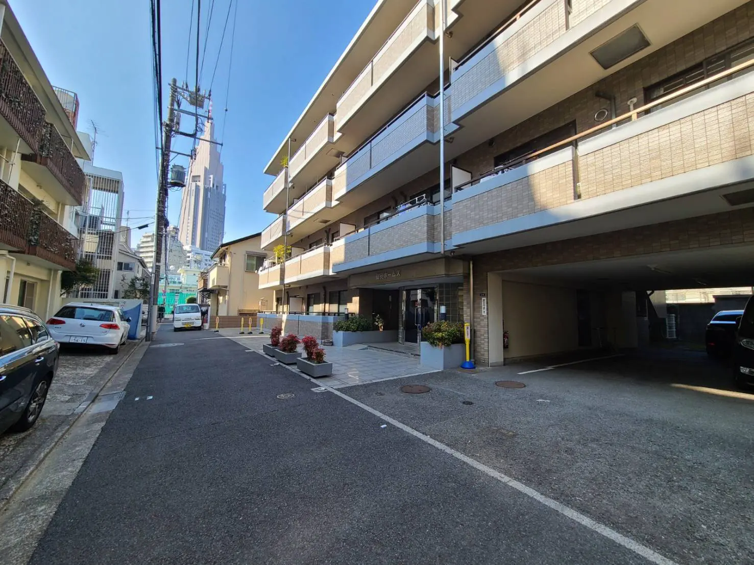 都市の住宅街の路地とアパート、晴れた空と高層ビルの見える風景