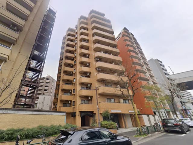 - 都市型マンションの外観、さまざまな高さの建物と車が並ぶ通り、緑の植栽と公園がある景観