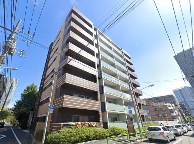 - 都市型のモダンなマンション外観、明るい青空と周囲の緑が映えるエリアの景観