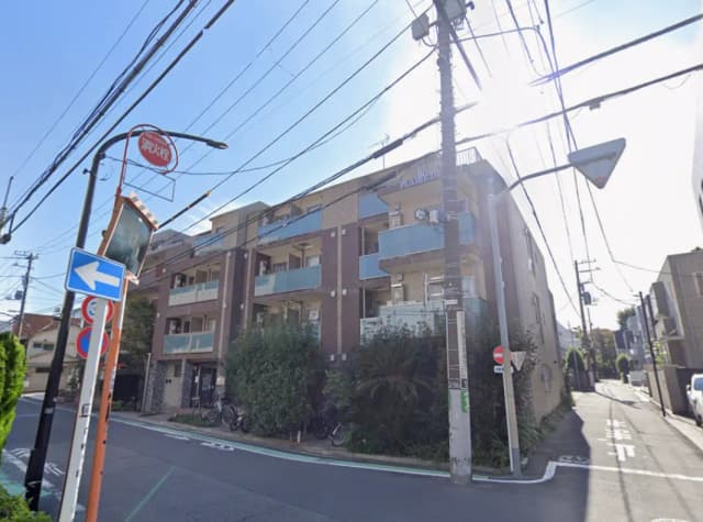 - アパートの外観、周囲には電柱や交通標識があり、青空が広がる街角の風景