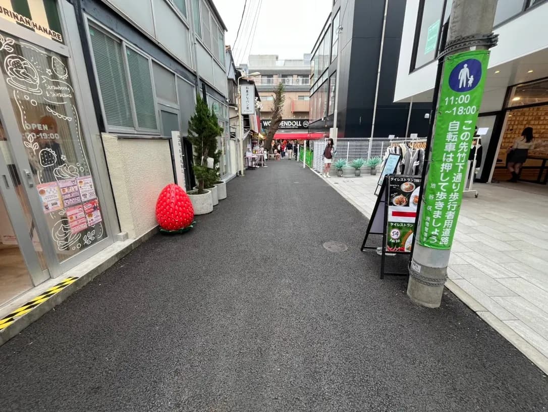 歩行者の通り、商店とレストランの店先、舗道に大きなイチゴのオブジェ、現代的な建物