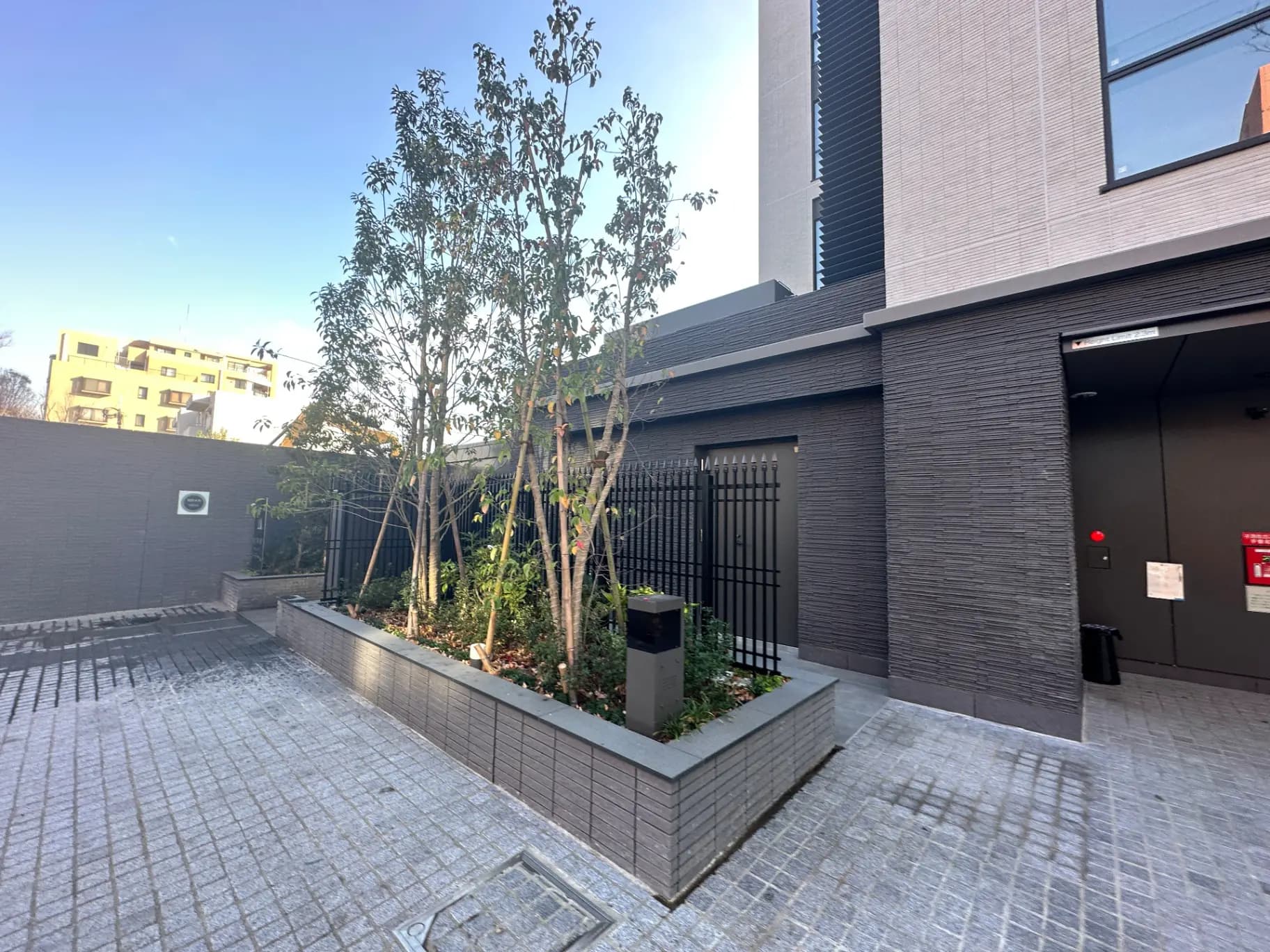 現代的な外観の建物入り口、駐車場付き、石畳と植栽が特徴的なエクステリアデザイン