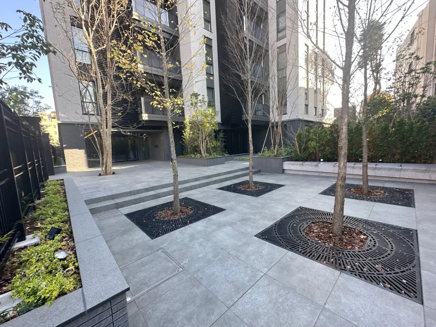 都市のモダンなビルのエントランスと緑の植栽、整然と配置された木と石畳の歩道