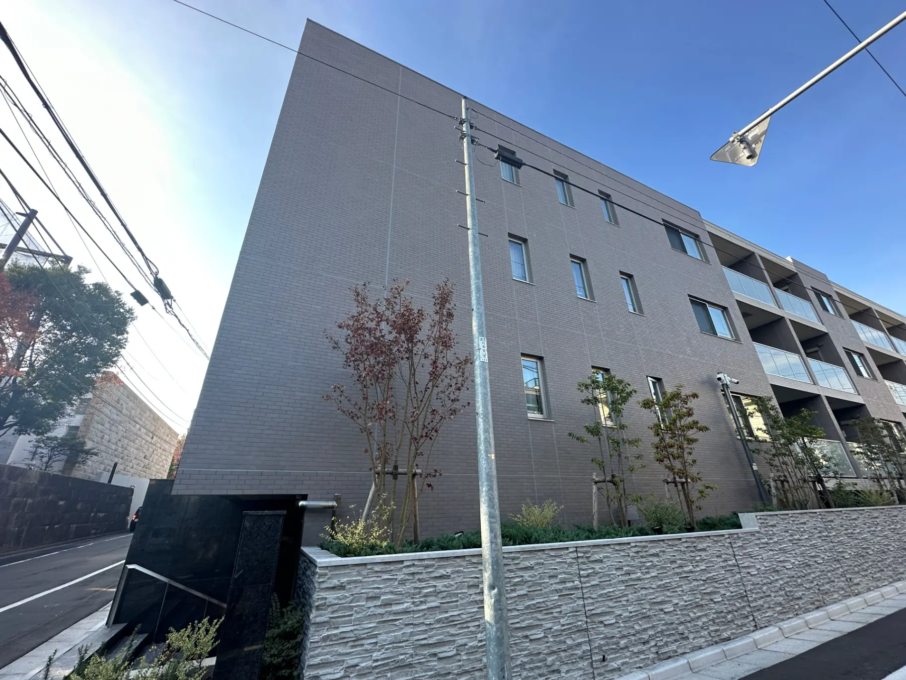 現代的なマンション外観、明るい日差しの下で街路樹と歩道が見える景観