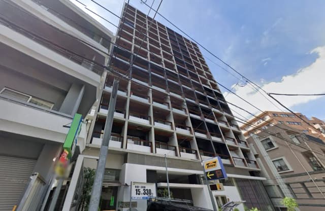 - モダンなデザインの外観を持つ高層ビル、近隣に駐車場の看板が見える街並みの風景