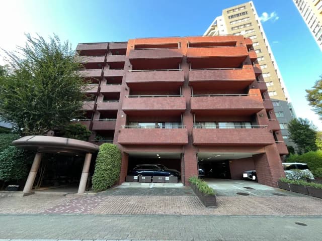 - 赤レンガの外観が特徴的なマンション、広々としたエントランス、駐車スペースと緑の植栽が整備された景観
