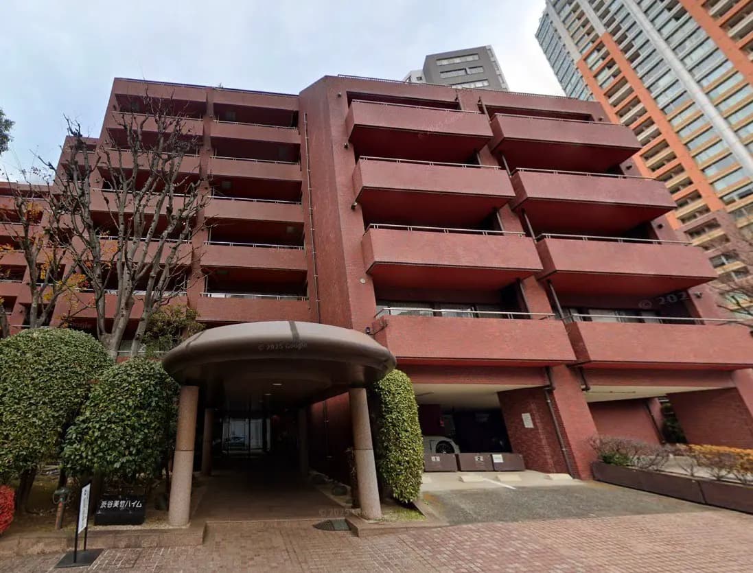 - 現代的なレンガ造りのマンション外観、エントランス周辺に植栽が施されたエリア、複数のバルコニーがある建物