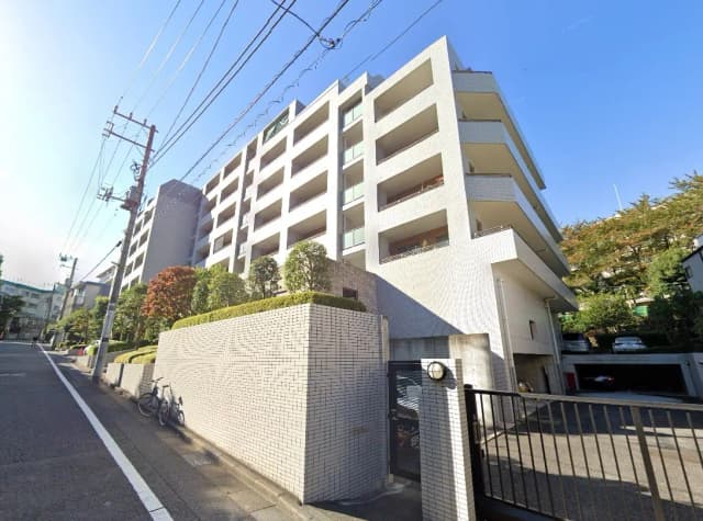 日当たりが良い都市のマンション外観、白いタイル壁、緑豊かな植栽がある門扉