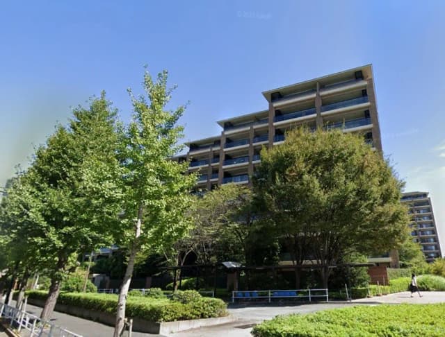 新緑に囲まれた都市部のモダンなマンション外観、晴天下での清潔感あふれる住宅街