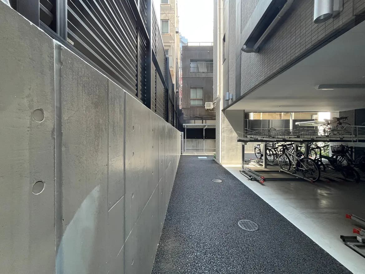 - 都市の駐輪場と舗装された通路、隣接するビルの壁と自転車ラックの様子
