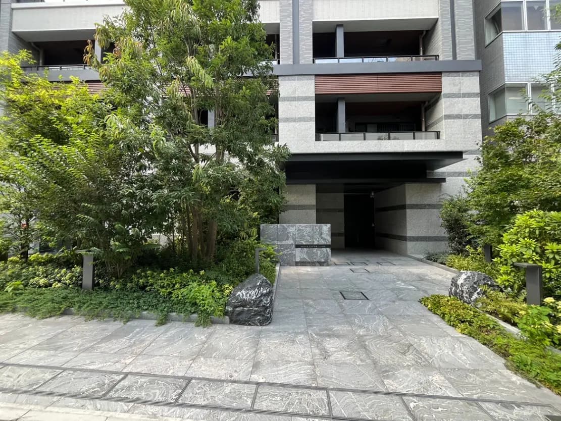 - モダンなアパートメントのエントランス、緑に囲まれた石畳の歩道と植栽が施された外観