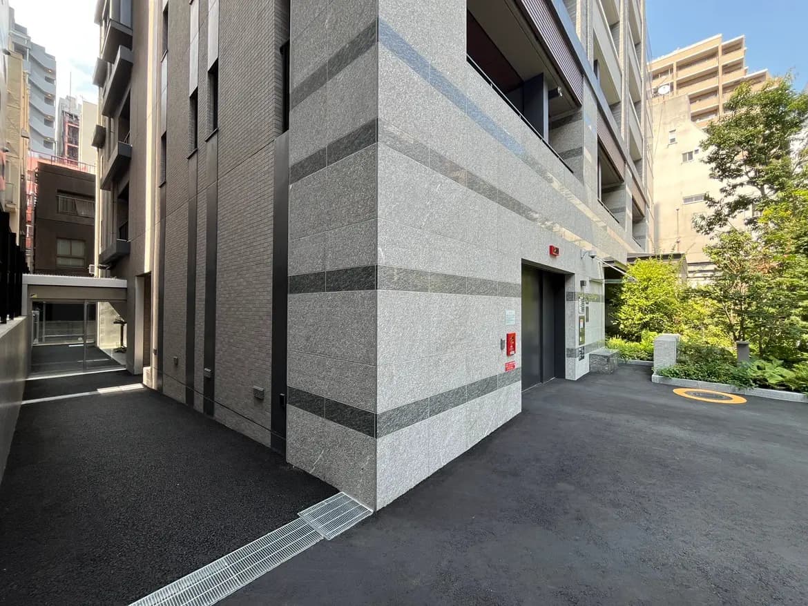 - グレーの外壁が印象的な現代的な建物のエントランス、周囲には緑が植えられた静かな空間と整備された歩道