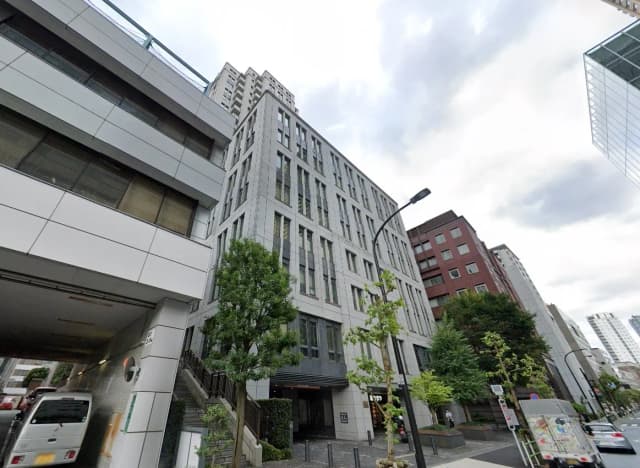現代的な建築デザインのオフィスビル、通り沿いに立つ樹木、曇り空の都市風景