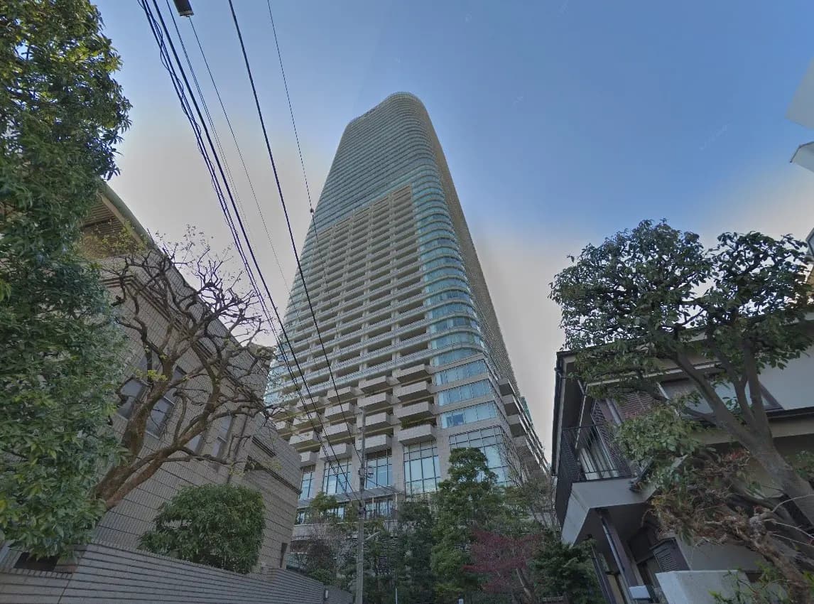 現代的な高層マンションが聳える都市の景観、周囲には木々と建物、青い空と都市生活