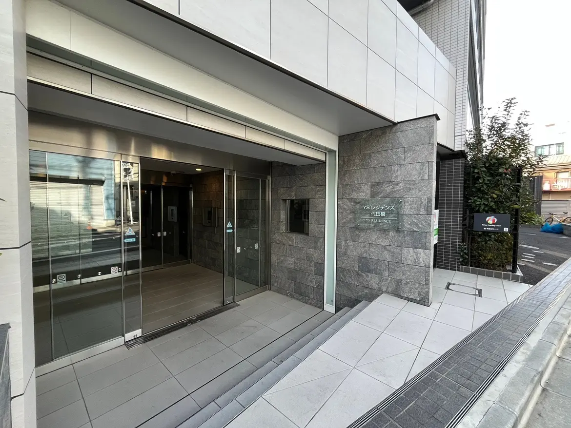 現代的なマンションのエントランス、ガラスドアと石造りの壁面デザイン
