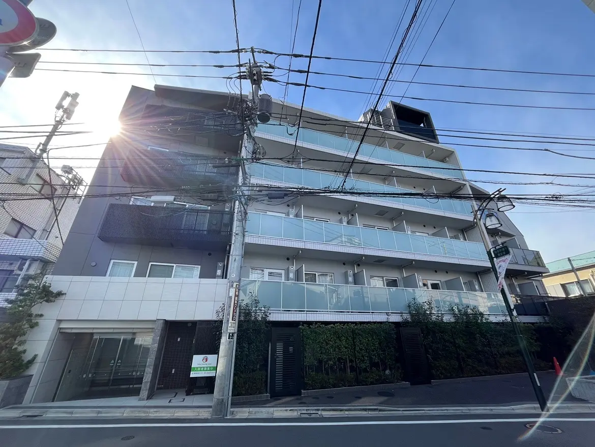 日差しが差し込む現代的なマンションの外観、道路沿いに配置された電柱と電線が目立つ都市の景観