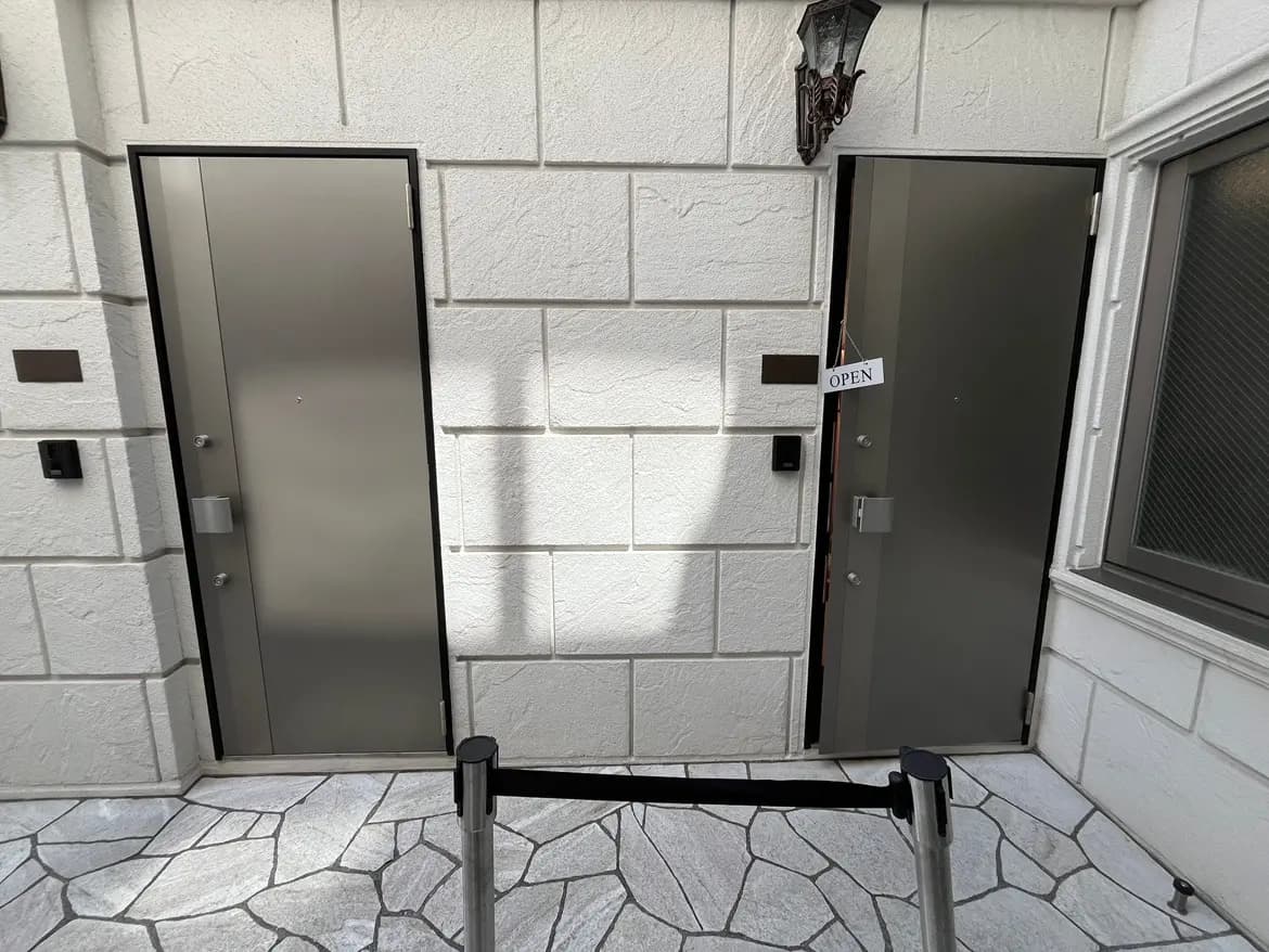 - 現代的なデザインのエントランス、メタリックなドアが2つ並び、片方には「OPEN」の看板が掛けられている外観の風景