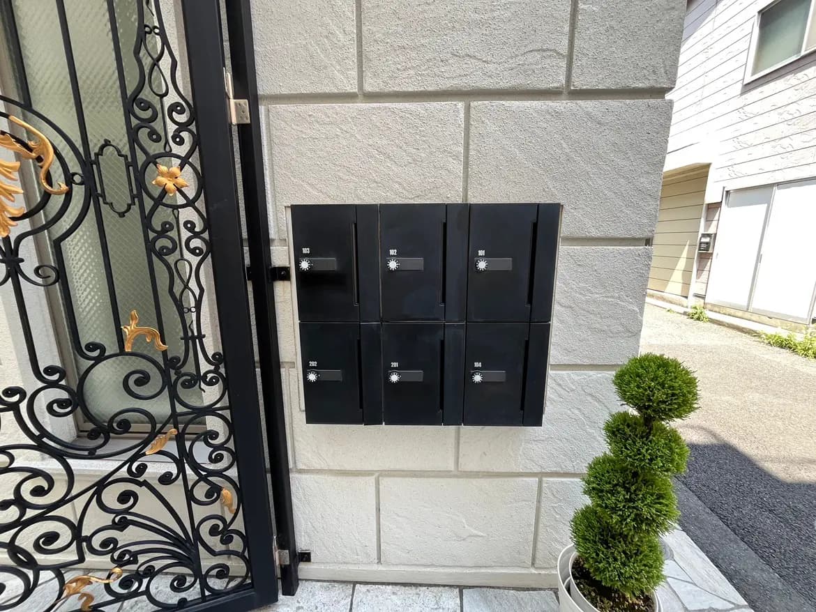 - モダンなデザインの郵便受けが施されたエントランスの壁、隣には小さな植栽が美しく配置されている風景