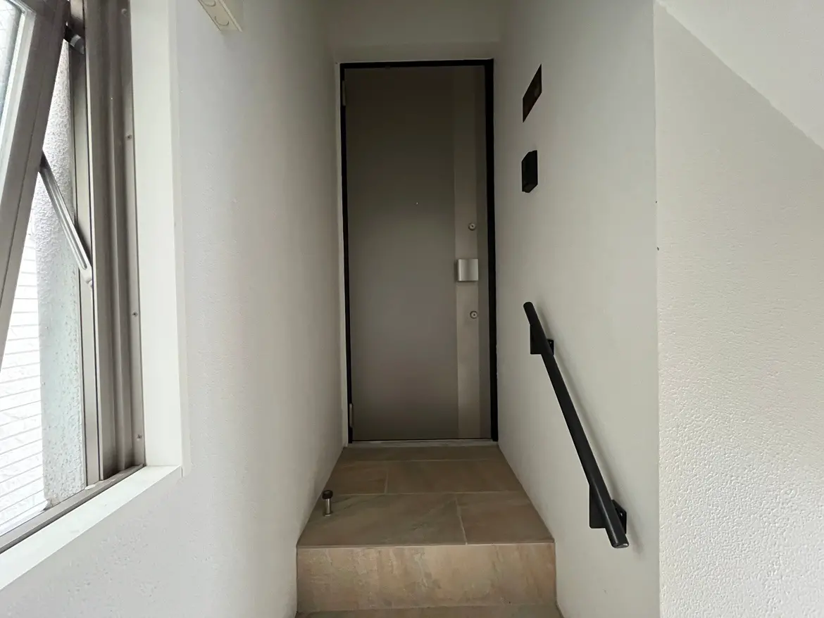 - シンプルなデザインの玄関アプローチ、階段と手すり、木製の扉と明るい壁の内装