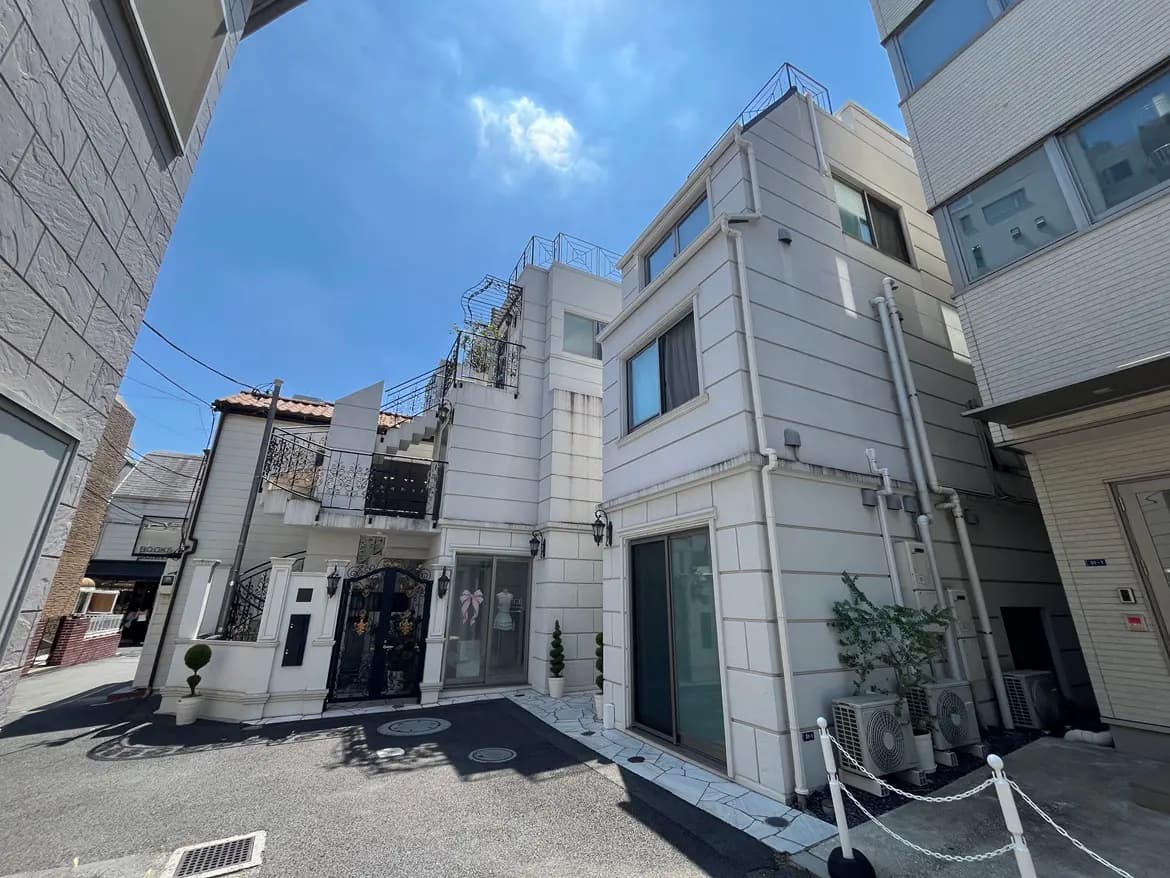 - 明るい青空の下、スタイリッシュな外観の住宅とその周辺、緑の植栽や階段のデザインが特徴的な街並み