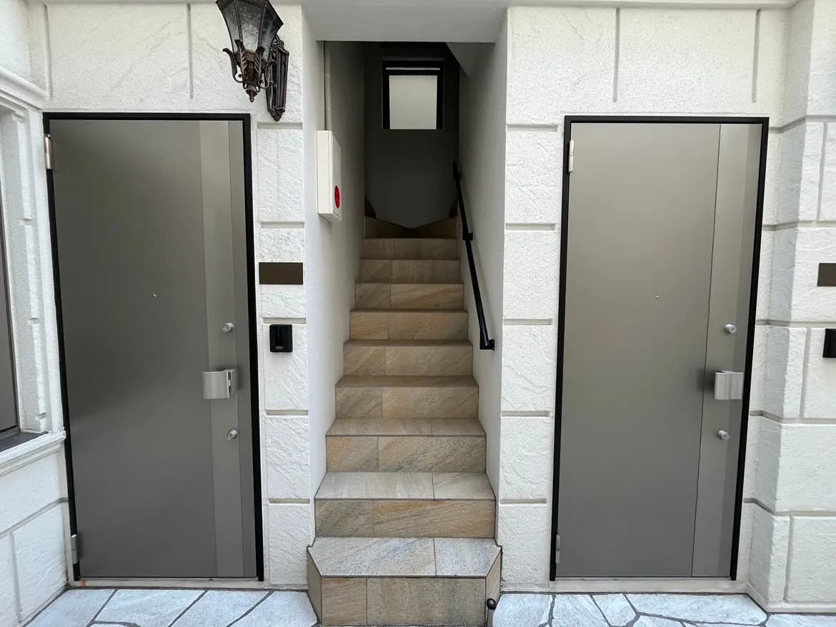 - モダンなアパートメントの玄関、左右に配置された灰色のドアと石造りの階段、アプローチに取り付けられた外灯があるエリア