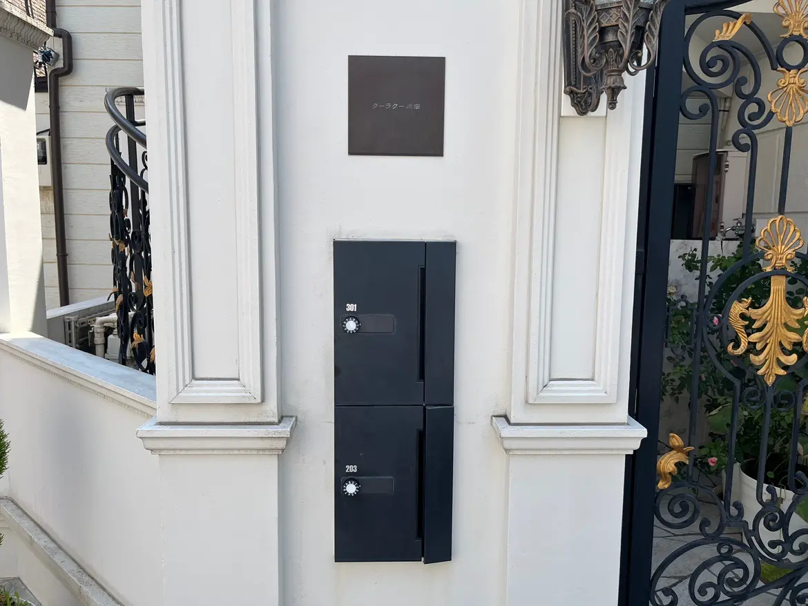 - モダンなデザインの郵便受けが壁に取り付けられた白い住宅の玄関、右側には豪華なゲートがある外観