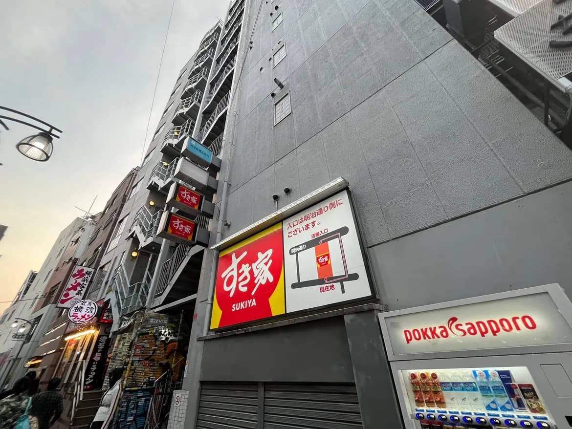 都会の雰囲気が感じられる飲食店が並ぶ通り、吹き抜けのある建物と外階段、看板には「すき家」と表示