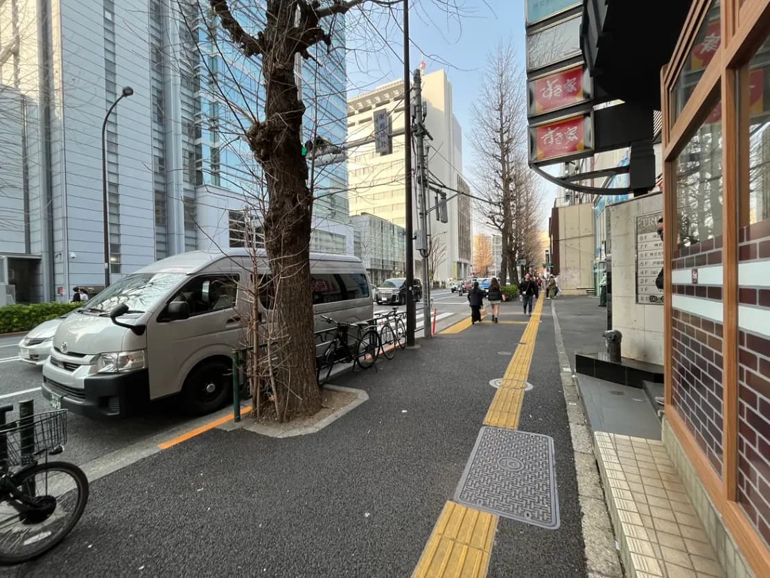 都会の通りと歩道、ビルと店舗が並ぶ景観、人々が歩く都市生活の一コマ