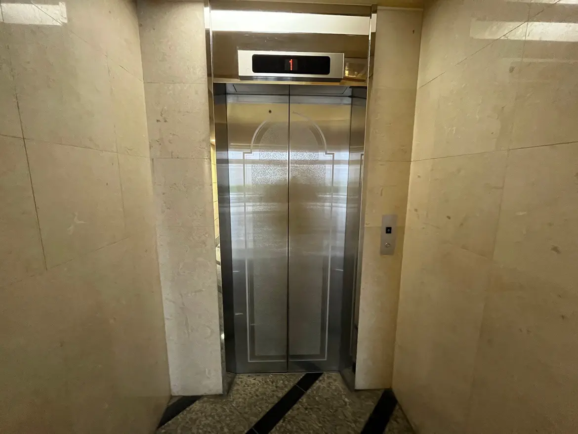 モダンな建物のエレベーター前、大理石風の壁面、閉じたエレベータードアとデジタル階数表示