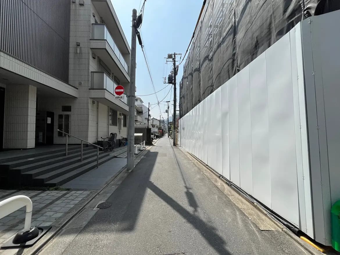晴れた日の日本の都市の狭い道路、建築中の建物の仮囲い、左側に現代的な建物と「進入禁止」標識