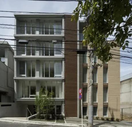 - 現代的なデザインの住宅ビル、ガラス面が広く明るく開放的な外観、緑の植栽と電線が見える都市の風景