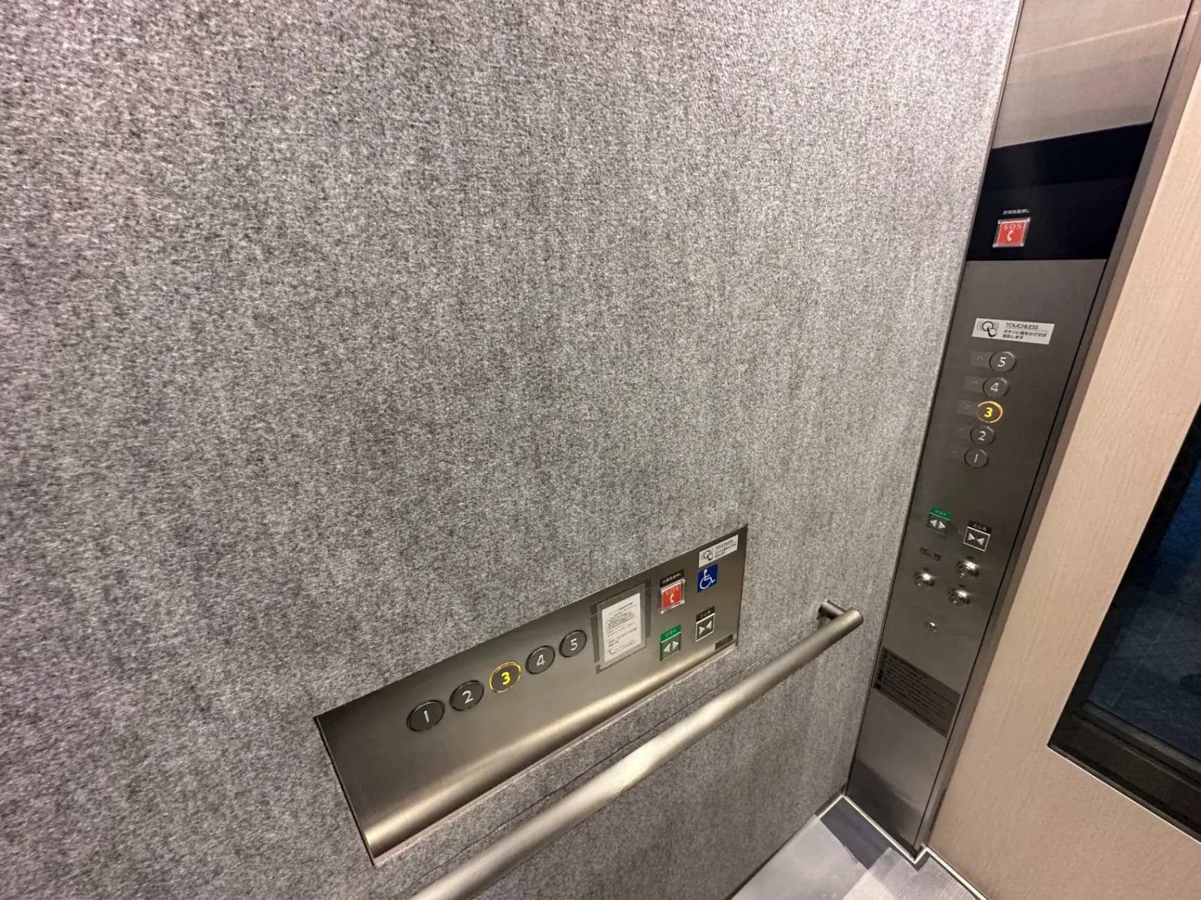 エレベーター内部のコントロールパネルとボタン、金属製の手すりとグレーの壁